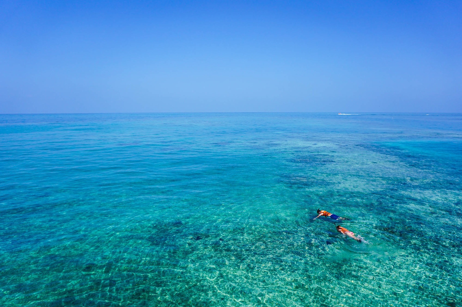 Dos personas disfrutan de su viaje por la India realizando buceo de superficie. Se ve un mar cristalino y a dos personas buceando en la superficie